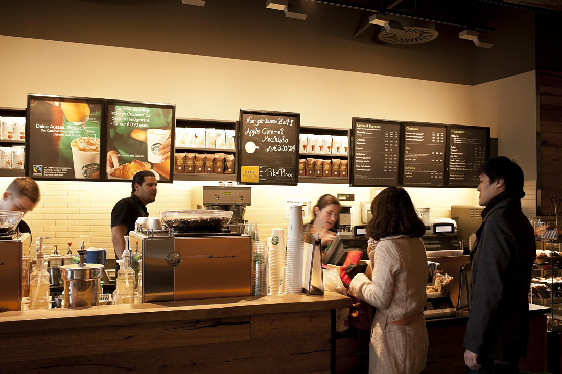 Illuminated Starbucks Coffee House counter in Koblenz with customers and staff.