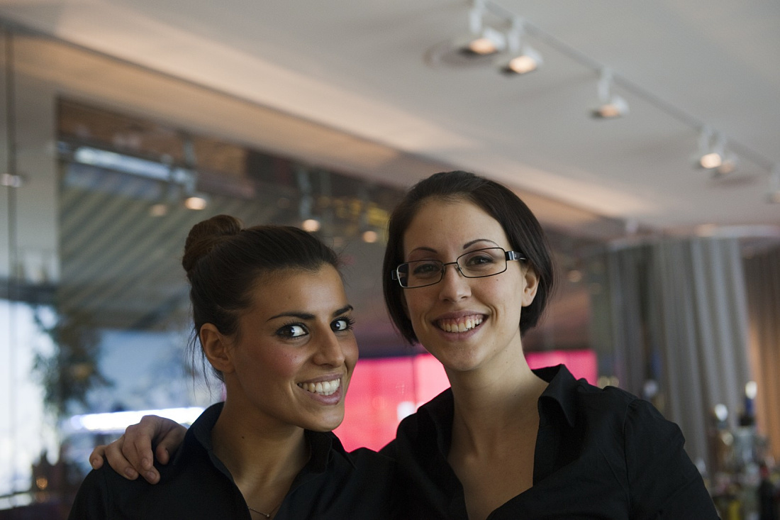 Two smiling women under ERCO Light Board spotlights at the Swiss Corner Bar, Milan.