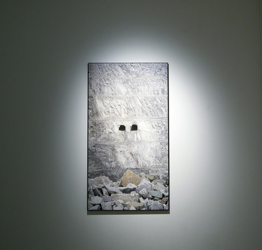 Kunsthalle Z33 exhibit: A photo of a rock wall with two dark holes, illuminated by ERCO spotlights.